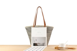 Detailed view of a striped woven straw tote bag with brown leather handles on a minimal desk