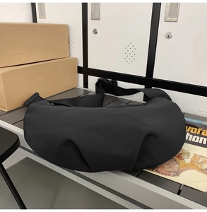 Large capacity black nylon crossbody dumpling bag shown in a casual lifestyle warehouse setting