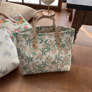 Detail of floral canvas tote bag with leather handles and metal rivets on wood floor