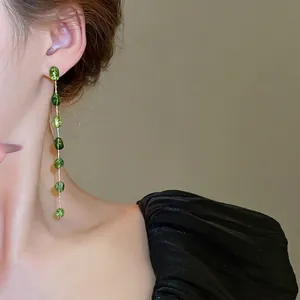 Long beaded drop earrings with silver chains and green translucent gemstones on a model