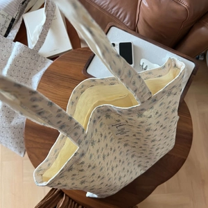Detailed view of beige canvas tote bag with floral pattern and stitched textile label