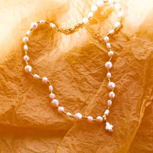 Collier de perles baroques avec pendentif croix et perles dorées sur papier texturé