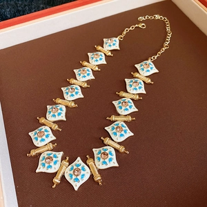 Close-up of vintage gold necklace with white enamel rhombus charms and pink gems in a gift box