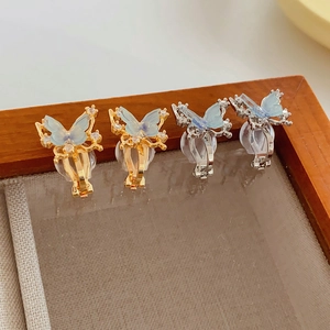 Detail of butterfly ear clips with blue resin wings and zircons on a beige jewelry tray