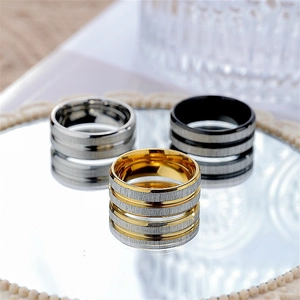 Brushed titanium steel rings in silver, black, and gold finishes on a mirror surface