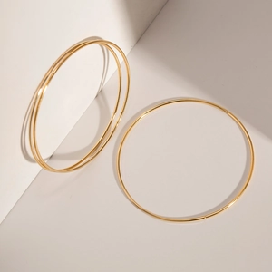Close-up of minimalist gold titanium steel bangles arranged with geometric shadows
