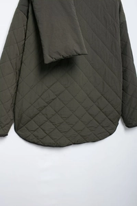 Close-up of deep green quilted jacket with diamond patterns and curved hem detail