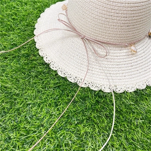 Détail d'un chapeau de paille d'été avec bords ondulés et décoration de ruban coquillage