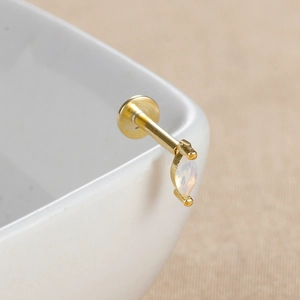 Détail macro du piercing labret en opale marquise dorée avec base plate en métal