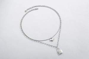 Detail of silver double-layered necklace featuring a heart charm and square lock pendant