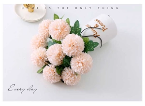 Close-up of artificial pink dandelion flower with green leaves in a white ceramic vase