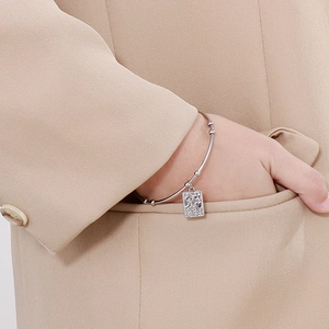 Detail of silver stainless steel thin bangle with rectangular engraved charm on model