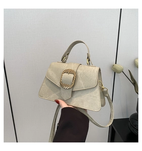 Detail of cream canvas handbag with gold metal buckle and leather handle held by hand
