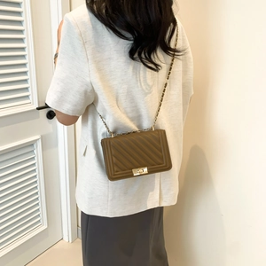 Detail view of the brown shoulder bag with V-shaped stitching and a metal twist lock