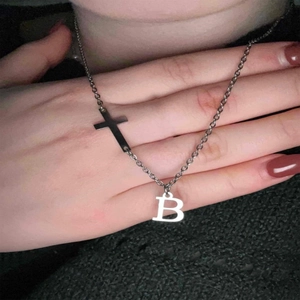 Detail shot of a silver metal cross necklace with letter B pendant on a neck