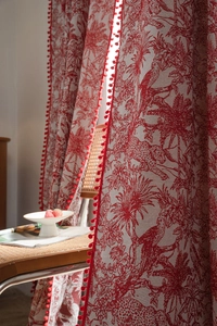 Detail of red forest print curtain with plush pom-pom trim and linen fabric texture
