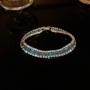 Vintage luxury gold bracelet with three rows of white and blue crystals on black background