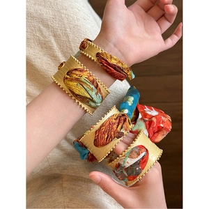 Close-up of matte gold open bangles with vintage silk ribbons and colorful patterns