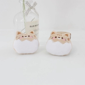 Close-up of cute plush cat brooches in creamy white and beige with delicate embroidery