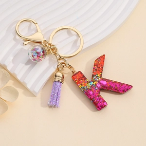 Detail of resin letter K keychain with pink sequins, purple tassel and golden clasp