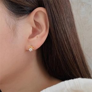 Close-up of a gold bow-knot stud earring with a sparkling round zircon on a model
