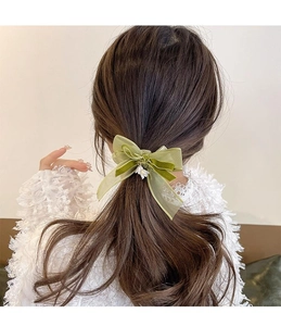 Detail of green bow hair tie with floral pendant on elegant textured velvet and gauze