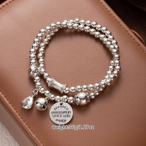 Close-up of multi-layer silver bead bracelet with dollar bag and bell charms on leather