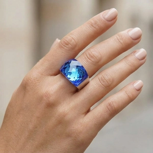 Close-up of a wide 18k gold-plated ring featuring a large faceted blue crystal stone