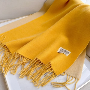 Detail of double-sided yellow and beige cashmere scarf with tassels and stitched label