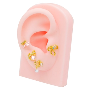 Golden stud earring set with cherry heart bow designs on pink silicone ear model
