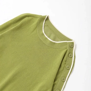 Green knit sweater with white trim and decorative shoulder buttons on a round neck