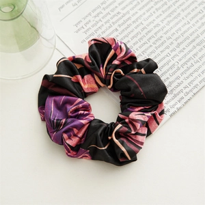 Close-up of a black scrunchie with purple and pink palm leaf patterns on a stylish background
