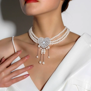 Detail showing triple-layer pearl necklace with sparkling heart pendant and elegant tassels