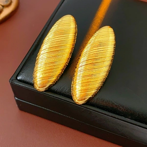 Macro detail of gold oval earrings featuring unique textured wire wrap design on a black box