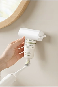 Detail of white wall-mounted toothpaste squeezer with rotary knob and electric toothbrush head