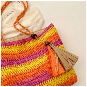 Detail of colorful striped straw beach bag with vibrant orange tassels and wooden beads
