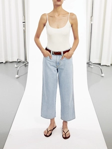 Detail of light blue high-waisted jeans styled with a white tank top and brown belt