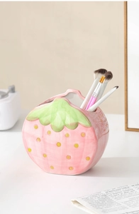 Detailed view of a cute pink ceramic strawberry holder storing makeup brushes on a desk