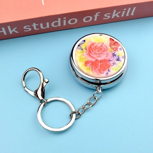 Detail of round portable pill box keychain with floral rose patterns and silver metal chain
