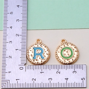Close-up of R and O letter charms in gold with blue and green enamel and ruler scale