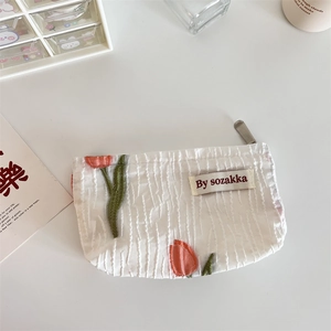 Close-up of plissé fabric makeup bag with red tulip embroidery and brand label