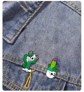 Close-up of enamel cactus skull pins on denim jacket showing punk style metal badge details