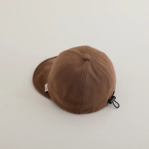 Detail of adjustable drawstring toggle and woven label on a brown twill baby baseball cap