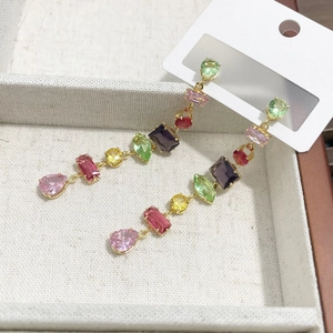 Elegant long gold earrings featuring multi-colored teardrop gems in a beige jewelry box