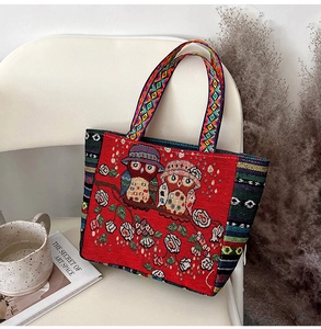 Detailed view of red ethnic tote bag with owl embroidery placed on a white chair