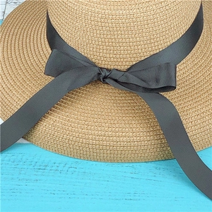 Close-up of wide charcoal ribbon bow on light brown woven straw sun hat surface