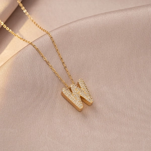 Close-up of gold-plated letter W necklace pendant with cubic zirconia on silk background
