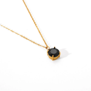 Detail view of gold necklace featuring a four-prong set round black gemstone pendant