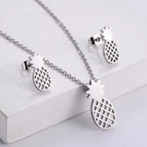 Silver hollow pineapple jewelry set featuring matching necklace and earrings on stone
