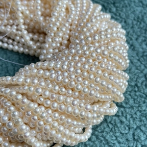 Strands of 4-5mm natural creamy white freshwater pearls on dark green velvet background